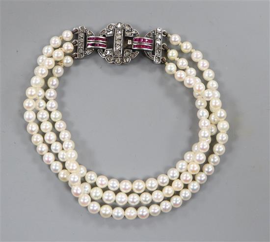 A triple strand cultured pearl bracelet with ruby and diamond set white metal clasp, 17cm.